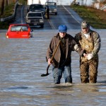 90-year-old Sid Staswick, left from Smokey Point, Wash., gets a helping hand through the floodwaters of the Stillaguamish River by Don Vanney after Staswick attempted to drive his red pick-up truck across the flooded roadway December 11, 2004 in Silvana, Wash.  Staswick was driving to his church to help them control the high water when he took the Pioneer Highway and got stuck in the rapidly rising waters.  He thought he could make it because he was “born in a flood in Silvana ninety years ago.”